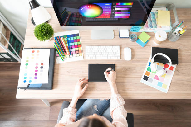 Top view of a woman using a graphic tablet and doing some design work in her workspace with many color palettes and swatches